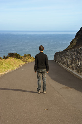 Portugal, Azoren, San Miguel, Mann steht auf der Straße und schaut auf das Meer, lizenzfreies Stockfoto