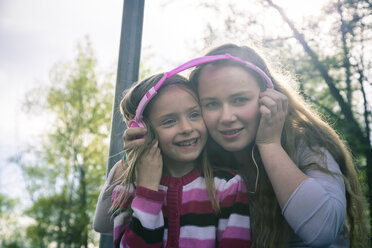 Zwei Schwestern mit rosa Kopfhörern hören gemeinsam Musik - SARF000554