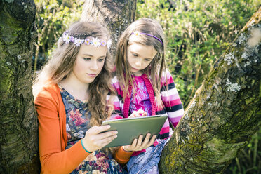 Two sisters with tablet computer together in garden - SARF000571