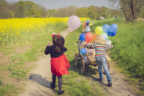 Drei Kinder unterwegs mit Holzwagen und Luftballons - MJF001094