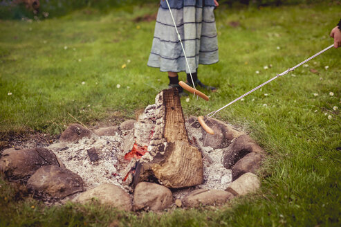 Mädchen grillt Würstchen am Lagerfeuer im Garten, Teilansicht - MJF001158