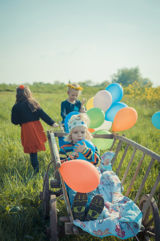 Drei Kinder unterwegs mit Holzwagen und Luftballons, lizenzfreies Stockfoto
