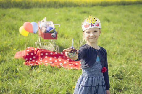 Porträt eines kleinen Mädchens mit Papier, das einen Geburtstagsmuffin anbietet, lizenzfreies Stockfoto