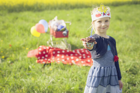 Porträt eines kleinen Mädchens mit Papier, das einen Geburtstagsmuffin anbietet - MJF001140