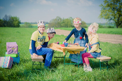 Vier Kinder mit Papierkronen feiern Geburtstag auf einer Wiese - MJF001143