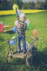 Little boy standing on wooden trolley holding ballons - MJF001144