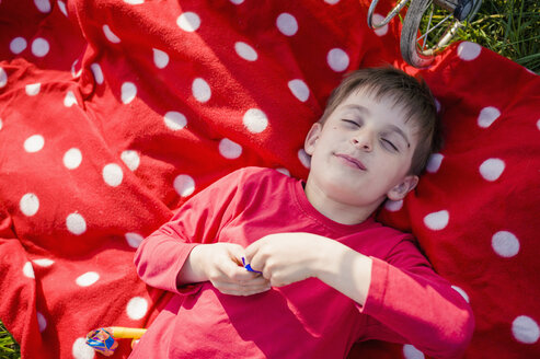 Lächelnder Junge mit geschlossenen Augen auf rot-weißer Polka-Dot-Decke liegend - MJF001146