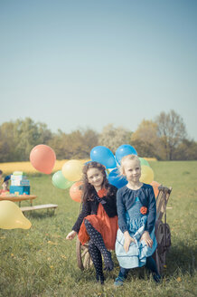 Zwei kleine Mädchen sitzen auf einem Holzwagen mit Luftballons - MJF001154