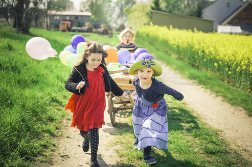 Drei Kinder unterwegs mit Holzwagen und Luftballons - MJF001162