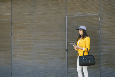 Spanien, Katalonien, Barcelona, junge moderne Frau mit gelber Jacke und Tablet-Computer wartet - EBSF000191