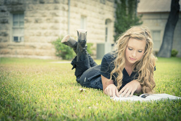 Portrait of young woman lying on grass reading a book - ABAF001342