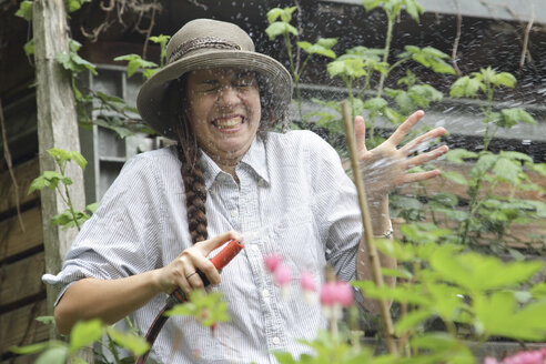 Junge Frau spritzt mit Wasser im Garten - SGF000619