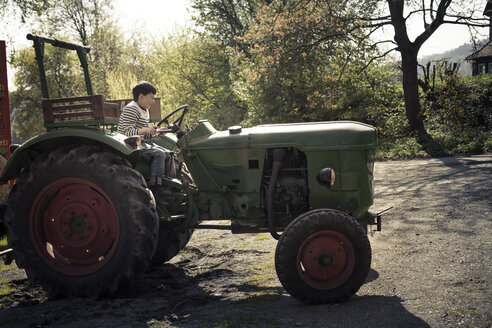 Deutschland, Nordrhein-Westfalen, Detmold, Lächelndes Kind auf Traktor, spielt mit dem Fahren - SBDF000810