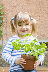 Portrait of smiling little girl holding flowerpot with basil - LVF001187