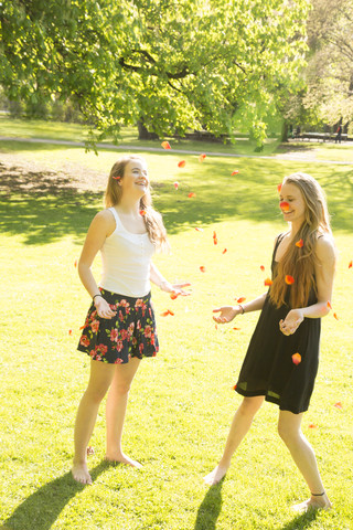 Zwei junge Freundinnen, die Blütenblätter in die Luft werfen, lizenzfreies Stockfoto