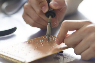 Electronic apprentice soldering circuit board at workshop, detail - SGF000638