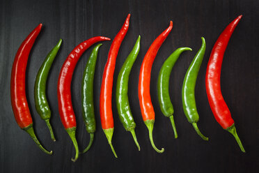 Row of red and green chili peppers on black ground - FCF000190