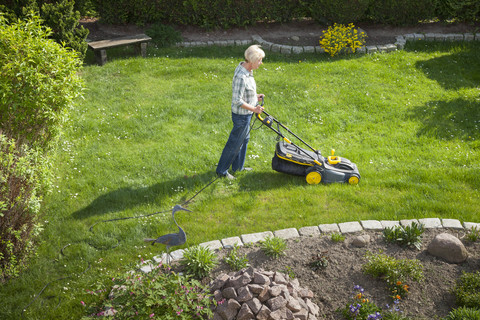 Deutschland, Frau mäht Rasen im Garten, lizenzfreies Stockfoto