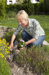 Deutschland, Frau pflanzt Blumen im Garten - WIF000626