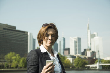 Germany, Hesse, Frankfurt, businesswoman watching her smartphone in front of skyline - UUF000467