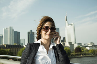 Germany, Hesse, Frankfurt, businesswoman telephoning with smartphone in front of skyline - UUF000469