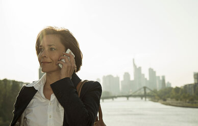 Germany, Hesse, Frankfurt, businesswoman telephoning with smartphone in front of skyline - UUF000470