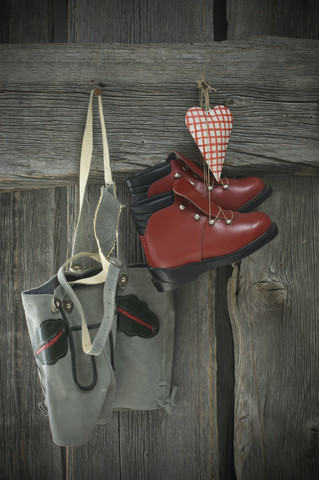 Lederhose, Skischuhe und Herz hängen an einer Holzwand, lizenzfreies Stockfoto