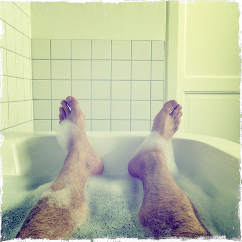 Mann in der Badewanne liegend, nur Füße sichtbar, lizenzfreies Stockfoto