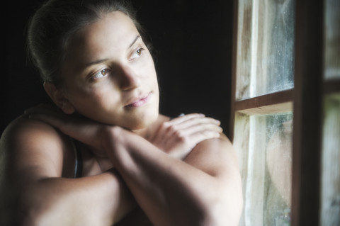 Junge Frau schaut durch ein Fenster, lizenzfreies Stockfoto