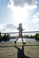 Junge Frau joggt über Brücke bei Gegenlicht - BFRF000406