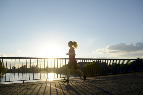 Junge Frau joggt über Brücke bei Gegenlicht - BFRF000416