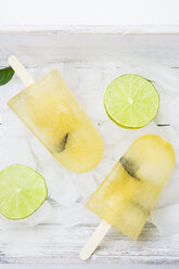 Two caipirinha ice lollies, ice cubes and slices of lime on white wood - LVF001221