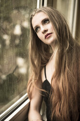 Porträt einer jungen Frau, die durch ein Fenster schaut - FCF000196