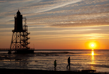 Deutschland, Niedersachsen, Dorum, Leuchtturm Obereversand und zwei Wanderer bei Sonnenuntergang - OLE000018