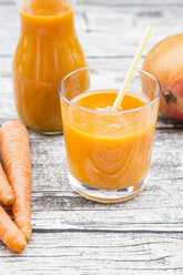 Glass and bottle of mango carrot smoothie on grey wood - LVF001236