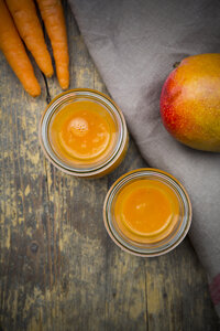 Zwei Gläser mit Mango-Karotten-Smoothie, Karotten und Mango auf Holztisch, Blick von oben - LVF001239