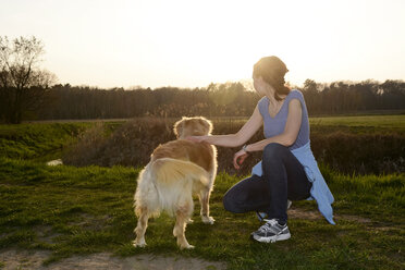 Junge Frau mit Golden Retriever auf einer Wiese bei Sonnenuntergang - BFRF000421