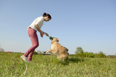 Junge Frau spielt mit Golden Retriever auf einer Wiese - BFRF000424