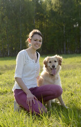 Junge Frau sitzt mit Golden Retriever auf einer Wiese - BFRF000425