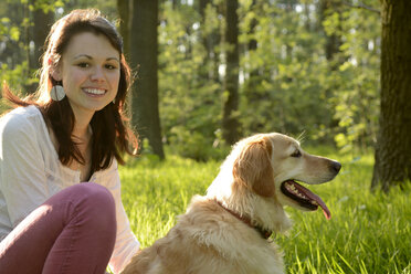 Portrait of young woman sitting with Golden Retriever on meadow - BFRF000432