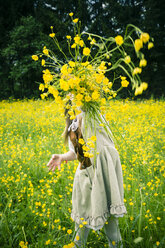 Kleines Mädchen in einem Kleid im Landhausstil wirft Butterblumen, Ranunkeln, in die Luft - SARF000595