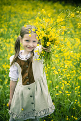 Little girl wearing country style dress presenting bunch of buttercups, Ranunculus, on meadow - SARF000596