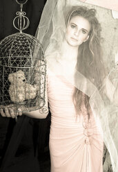 Young woman with teddy bear in bird cage wearing evening dress - FCF000203