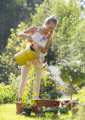 Laughing teenage girl watering potted plants in the garden - WWF003295