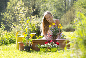 Portrait of smiling teenage girl repotting plants in the garden - WWF003296