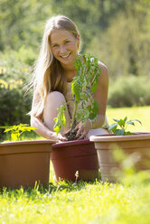 Portrait of smiling teenage girl repotting plant in the garden - WWF003299