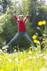 Glückliches Teenager-Mädchen, das auf einer Blumenwiese in die Luft springt - WWF003303