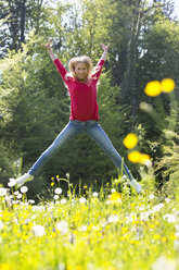 Happy teenage girl jumping in the air on a flower meadow - WWF003303