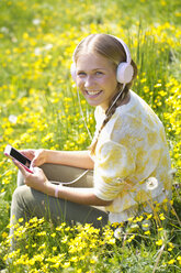 Porträt eines lächelnden Teenagers mit Kopfhörern, der auf einer Blumenwiese Musik hört - WWF003306