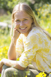 Porträt eines lächelnden Teenagers, der auf einer Blumenwiese sitzt - WWF003307